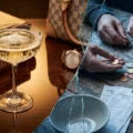 A glass of champagne and wealth books contrast with poor hands counting coins, divided by broken glass.